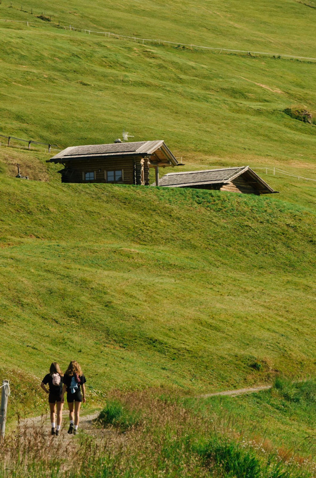 Two people walking a path toward a cabin in green hills